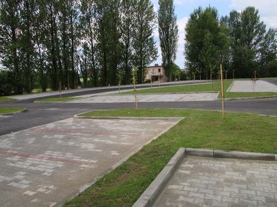 Zdjęcie przedstawiające widok na nową asfaltową drogę oraz miejsca parkingowe a w tle drzewa.