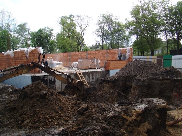 Budowa sali gimnastycznej - na zdjęciu fragment budowy, maszyna budowlana oraz zieleń