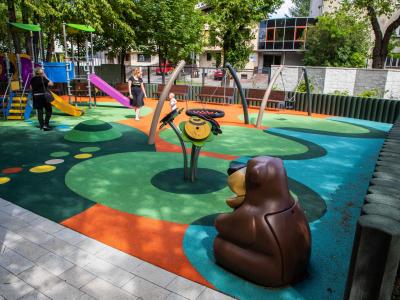 Zdjęcie przedstawiające kolorowy plac zabaw z huśtawkami, zjeżdżalniami i figurką misia.