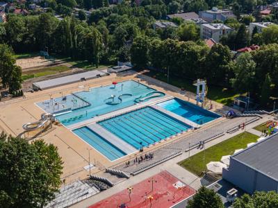 Zdjęcie przedstawiające kompleks odkrytych basenów przy ul. Marii Konopnickiej w Bielsku-Białej z brodzikiem, zjeżdżalniami i trybunami, widziany z lotu ptaka.