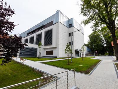 Zdjęcie przedstawiające nowoczesny budynek z białą elewacją otoczony alejkami i zielenią.