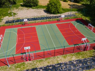 Zdjęcie przedstawiające wielofunkcyjne boisko sportowe z bramkami i koszami z lotu ptaka.