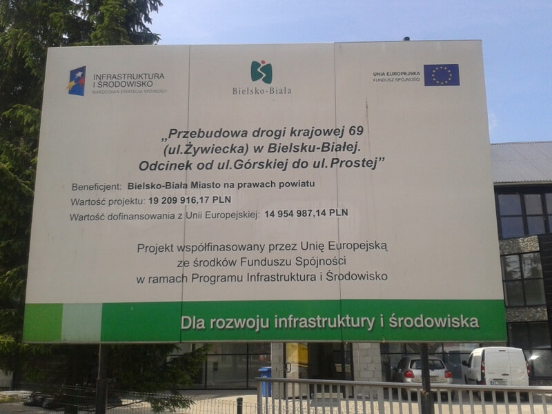 Przebudowa drogi krajowej 69 - na zdjęciu tablica informacyjna, w tle budynek oraz zieleń