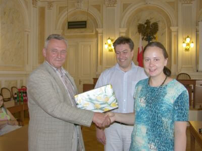 Zdjęcie uścisku dłoni podczas wręczania upominku w sali z orłem i flagą Polski.