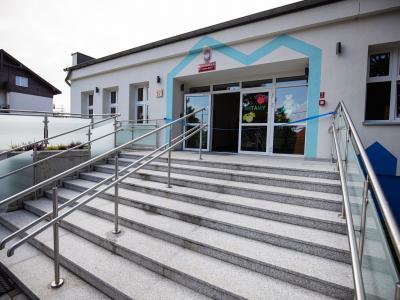 Zdjęcie przedstawiające wejście do budynku publicznego z podjazdem i schodami.