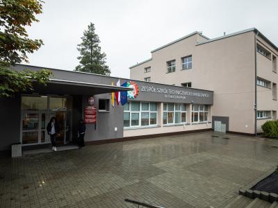 Zdjęcie przedstawiające wejście do zespołu szkół technicznych z widocznym szyldem i flagami.