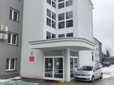 Zdjęcie przedstawiające wejście do budynku użyteczności publicznej z przeszklonymi drzwiami i zadaszeniem.