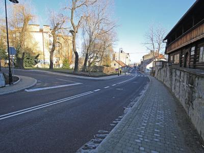 Zdjęcie przedstawiające nową nawierzchnię asfaltową i chodnik pomiędzy zabytkowy drewnianym budynkiem oraz inną zabudową miejską.
