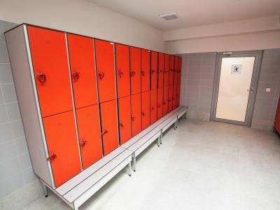 Zdjęcie przedstawiające szatnie z rzędem czerwonych szafek i ławką.