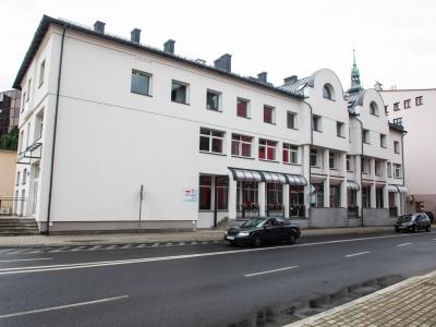 Zdjęcie przedstawiające budynek Urzędu Miejskiego w Bielsku-Białej przy ul. Stanisława Stojałowskiego 32 o białej elewacji od strony ulicy. 