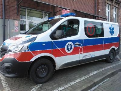 Zdjęcie przedstawiające karetkę transportową na tle budynku.
