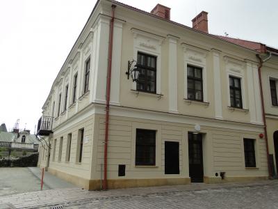 Zdjęcie przedstawiające zabytkową narożną kamienicę z jasną elewacją i brukowanym chodnikiem.