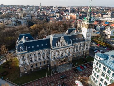 Zdjęcie przedstawiające zabytkowy ratusz z wieżą zegarową, widziany z lotu ptaka na tle miasta.