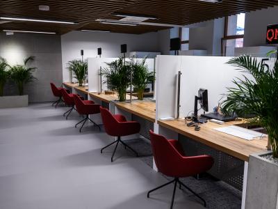 Zdjęcie przedstawiające nowoczesne stanowiska obsługi klienta z komputerami i czerwonymi krzesłami.