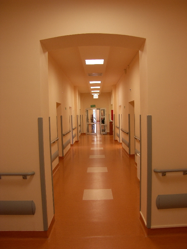 na zdjęciu jasny szpitalny korytarz z poręczami wzdłuż ścian i drzwiami do sal