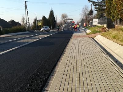 Zdjęcie przedstawiające układanie nowej nawierzchni asfaltowej obok chodnika z kostki brukowej..