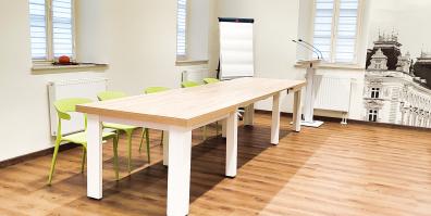 zdjęcie przedstawiające sale ze stołem, krzesłami, flipchartem oraz mównicą