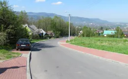 Przebudowa ul. Ks. Brzóski w Bielsku-Białej - na zdjęciu fragment drogi, budynki, chodniki, samochód oraz zieleń