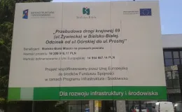 Przebudowa drogi krajowej 69 - na zdjęciu tablica informacyjna, w tle budynek oraz zieleń