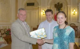 Zdjęcie uścisku dłoni podczas wręczania upominku w sali z orłem i flagą Polski.