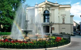 zdjęcie przedstawiające front budynku Teatru Polskiego w Bielsku-Białej w otoczeniu zieli i fontanny z kwiatami