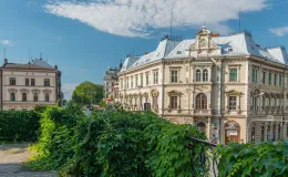 Zdjęcie przedstawiające widok na kamienicę przy skrzyżowaniu ul. 3-go Maja oraz ul. Stanisława Stojałowskiego oraz balustrade obrośniętą zielenią.  