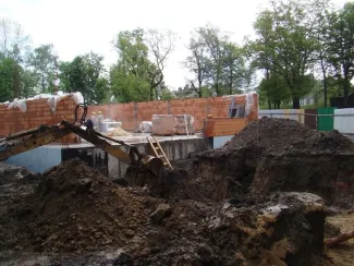 Budowa sali gimnastycznej - na zdjęciu fragment budowy, maszyna budowlana oraz zieleń