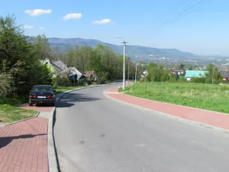 Przebudowa ul. Ks. Brzóski w Bielsku-Białej - na zdjęciu fragment drogi, budynki, chodniki, samochód oraz zieleń