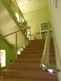 na zdjęciu schody wewnętrzne z poręczą i zielonymi ścianami prowadzące na piętro