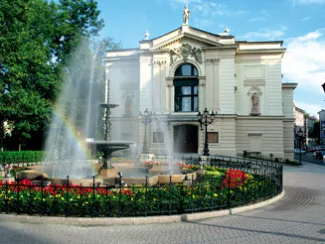 zdjęcie przedstawiające front budynku Teatru Polskiego w Bielsku-Białej w otoczeniu zieli i fontanny z kwiatami