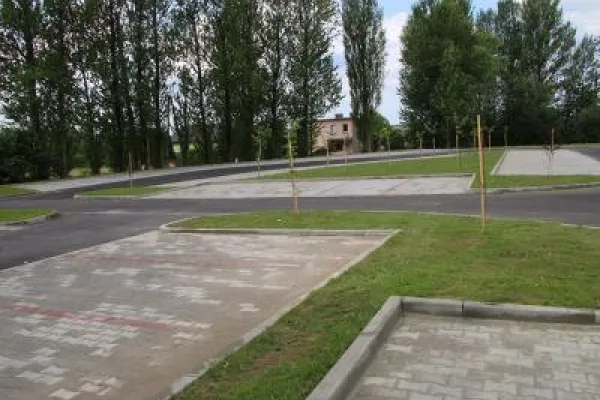 Zdjęcie przedstawiające widok na nową asfaltową drogę oraz miejsca parkingowe a w tle drzewa.
