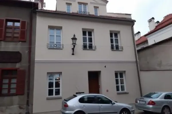 Zdjęcie przedstawiające niewielką kamienicę z jasną elewacją przy pl. św. Mikołaja 12 i zaparkowanymi przed nią samochodami