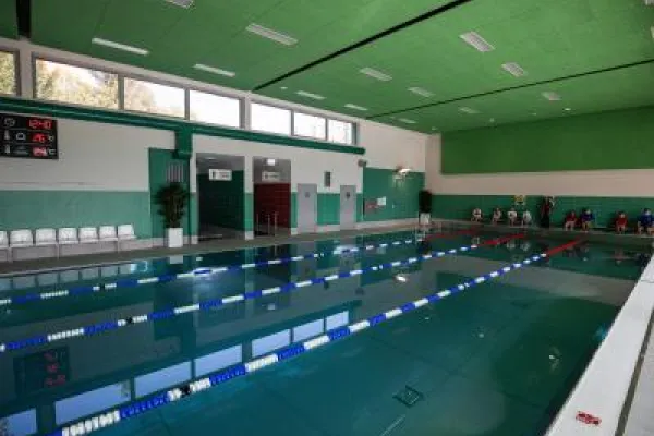 Zdjęcie przedstawiające kryty basen pływacki z torami i zielonym sufitem.