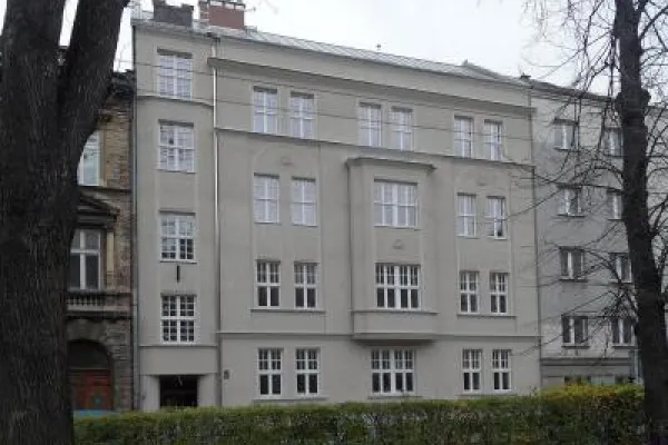 Zdjęcie przedstawiające odnowioną kamienicę z jasną elewacją, częściowo zasłoniętą drzewami.