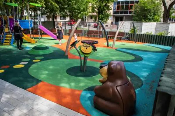 Zdjęcie przedstawiające kolorowy plac zabaw z huśtawkami, zjeżdżalniami i figurką misia.