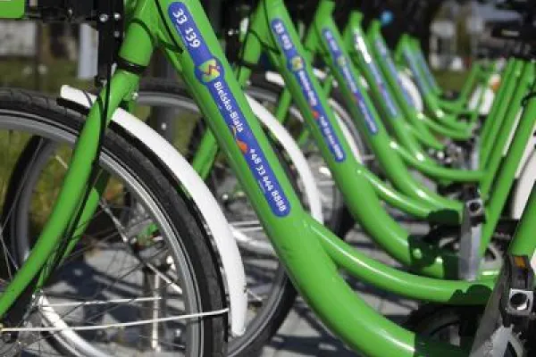 Zdjęcie przedstawiające rząd zielonych rowerów miejskich na stacji wypożyczeń.