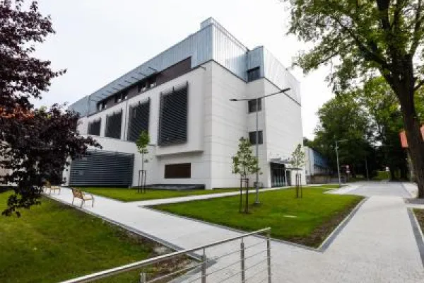 Zdjęcie przedstawiające nowoczesny budynek z białą elewacją otoczony alejkami i zielenią.