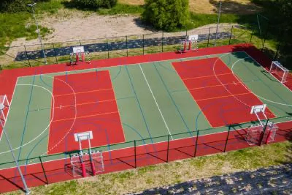Zdjęcie przedstawiające wielofunkcyjne boisko sportowe z bramkami i koszami z lotu ptaka.