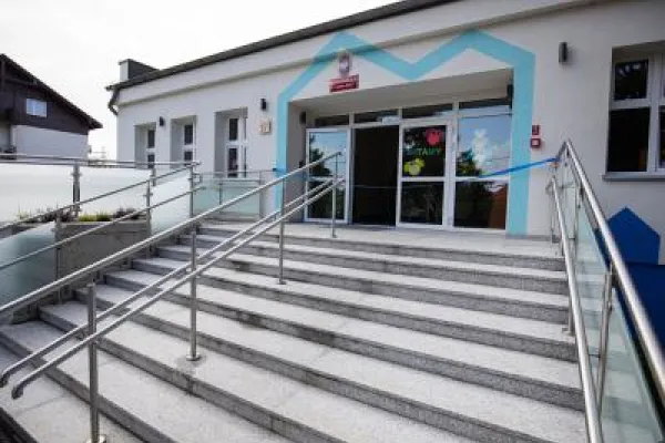 Zdjęcie przedstawiające wejście do budynku publicznego z podjazdem i schodami.
