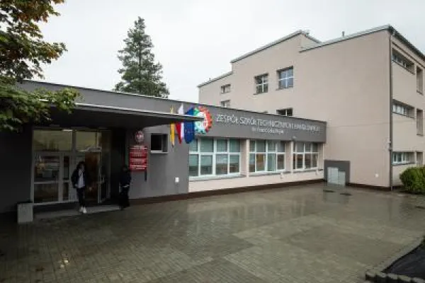 Zdjęcie przedstawiające wejście do zespołu szkół technicznych z widocznym szyldem i flagami.