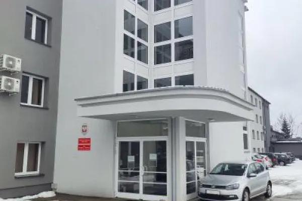 Zdjęcie przedstawiające wejście do budynku użyteczności publicznej z przeszklonymi drzwiami i zadaszeniem.