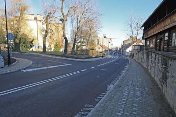 Zdjęcie przedstawiające nową nawierzchnię asfaltową i chodnik pomiędzy zabytkowy drewnianym budynkiem oraz inną zabudową miejską.