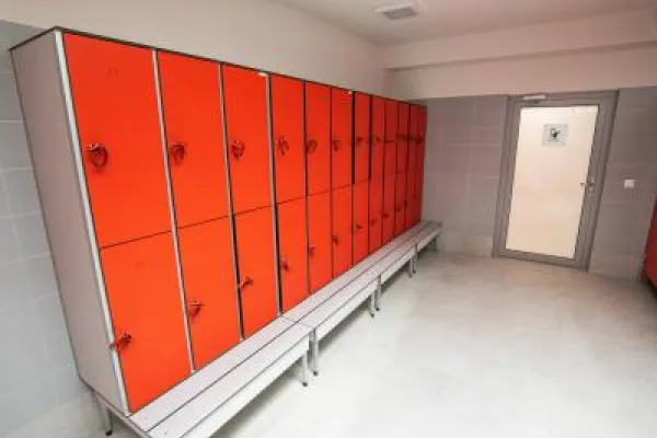 Zdjęcie przedstawiające szatnie z rzędem czerwonych szafek i ławką.