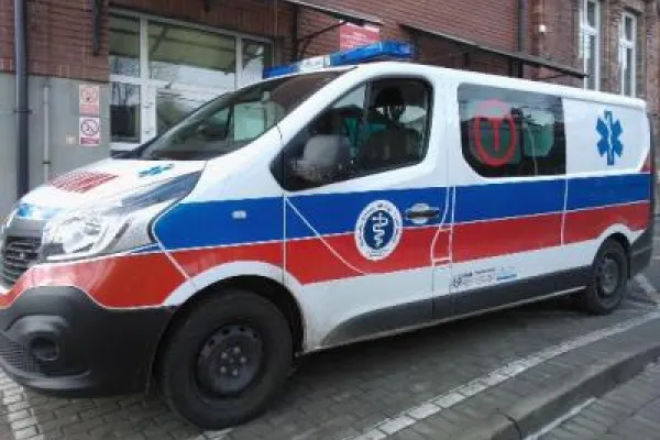 Zdjęcie przedstawiające karetkę transportową na tle budynku.