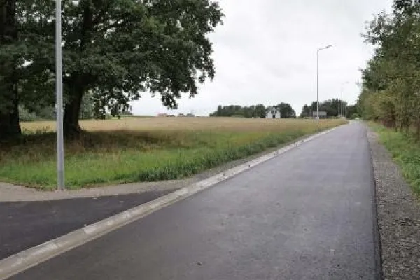 Zdjęcie przedstawiające nową asfaltową drogę biegnącą wzdłuż pola i drzew.
