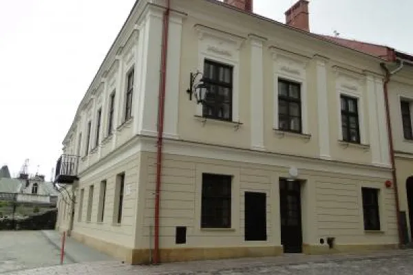 Zdjęcie przedstawiające zabytkową narożną kamienicę z jasną elewacją i brukowanym chodnikiem.