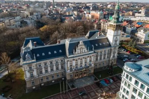 Zdjęcie przedstawiające zabytkowy ratusz z wieżą zegarową, widziany z lotu ptaka na tle miasta.