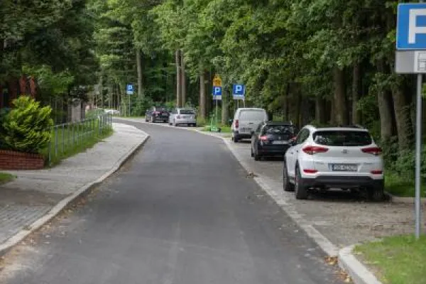 Zdjęcie przedstawiające ulicę z miejscami parkingowymi wzdłuż chodnika, otoczoną drzewami.