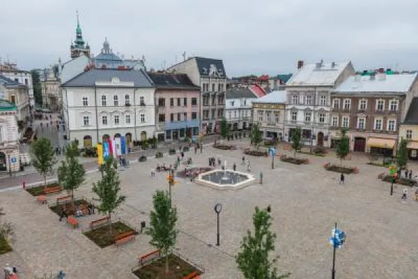 Zdjęcie przedstawiające Plan Wojska Polskiego w Bielsku-Białej z fontanną, drzewami, ławkami i zabytkowymi kamienicami wokół.
