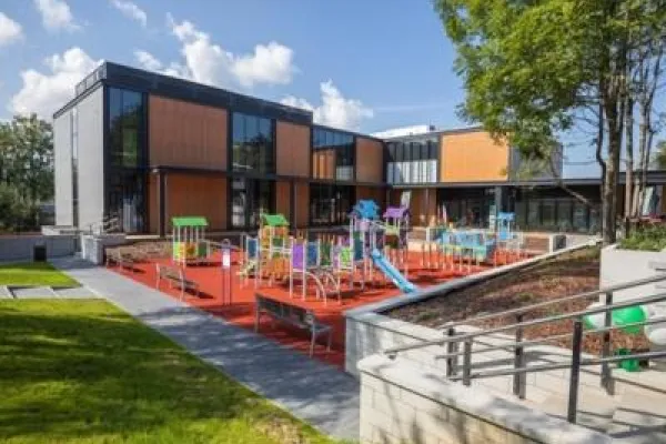 Zdjęcie przedstawiające kolorowy plac zabaw przy nowoczesnym budynku z dużymi oknami.